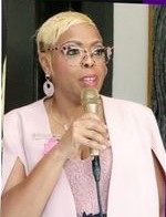 Woman in pink top speaking, with microphone in right hand
